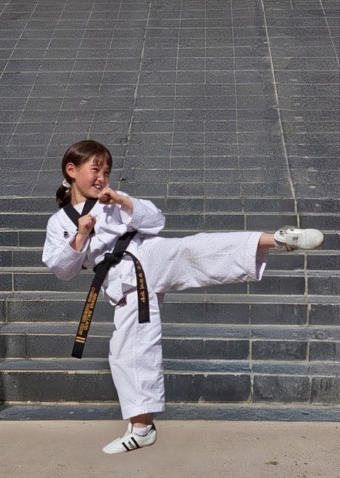 A student in a KAT dobok holding a side kick on outdoor steps